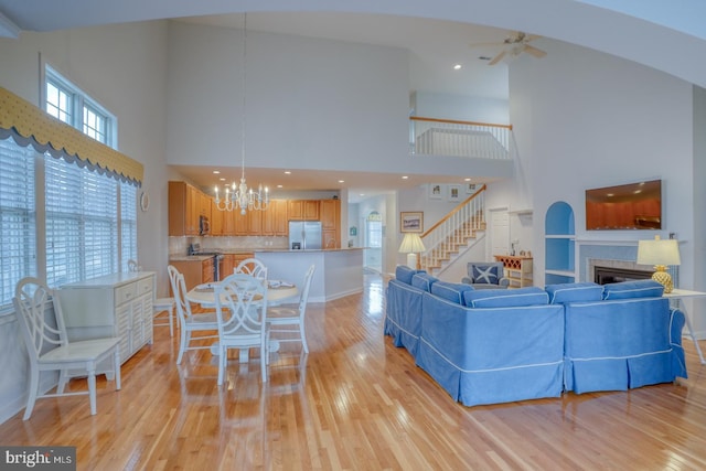 living room featuring light hardwood / wood-style flooring, a towering ceiling, ceiling fan with notable chandelier, and a brick fireplace