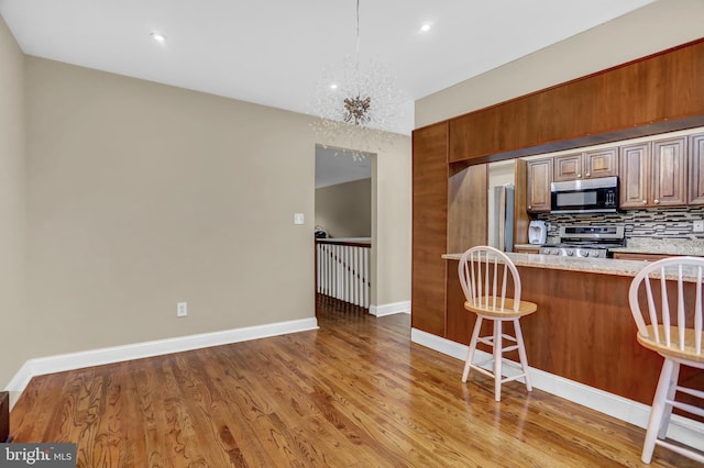 kitchen with stainless steel appliances, tasteful backsplash, light hardwood / wood-style flooring, a notable chandelier, and a breakfast bar area