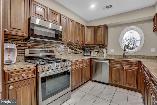 kitchen featuring backsplash, stainless steel appliances, light stone counters, and sink