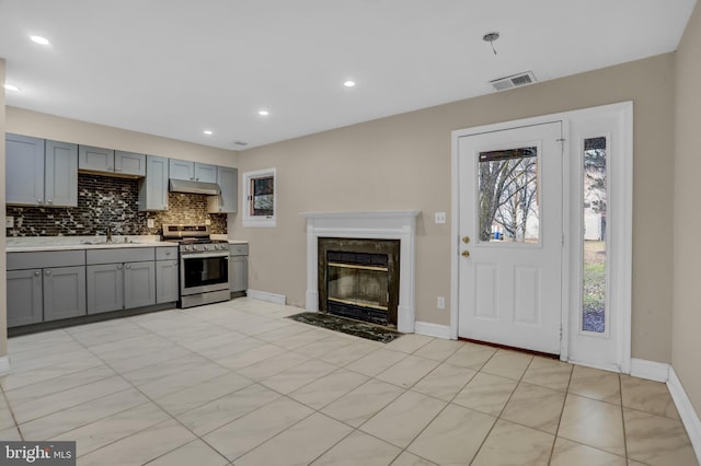 kitchen featuring sink, a premium fireplace, stainless steel range oven, gray cabinets, and decorative backsplash