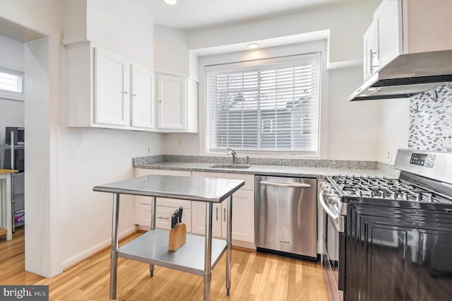 kitchen with wall chimney range hood, sink, light hardwood / wood-style flooring, appliances with stainless steel finishes, and white cabinetry