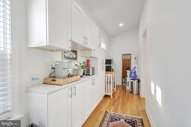 kitchen with white cabinets, vaulted ceiling, and light wood-type flooring