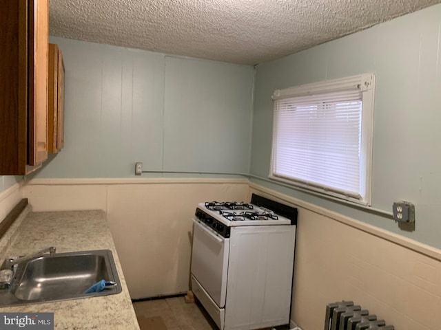 kitchen with a textured ceiling, white range with gas stovetop, sink, and radiator