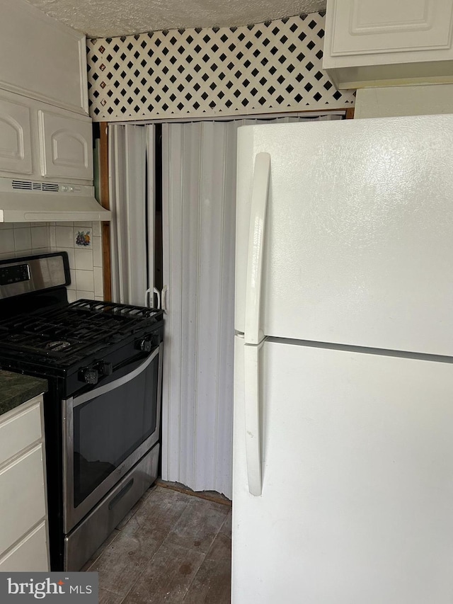 kitchen featuring stainless steel gas range, tasteful backsplash, range hood, white refrigerator, and white cabinets