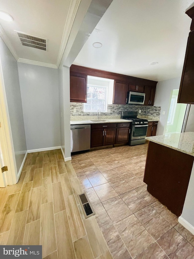 kitchen with backsplash, sink, ornamental molding, appliances with stainless steel finishes, and light stone counters