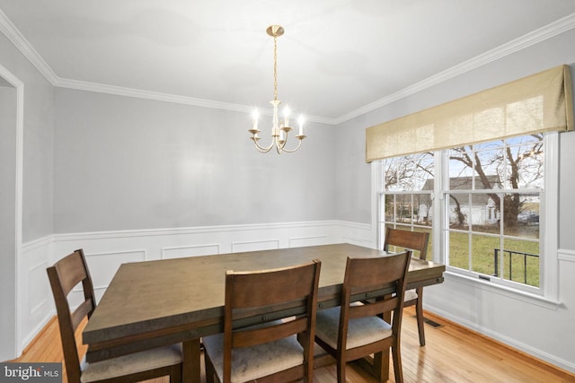 dining area with a notable chandelier, ornamental molding, and light hardwood / wood-style flooring