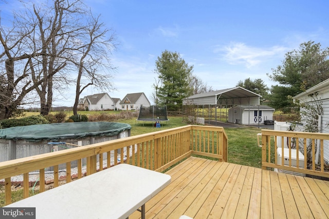 wooden deck featuring a lawn, a trampoline, a carport, a storage shed, and a covered pool