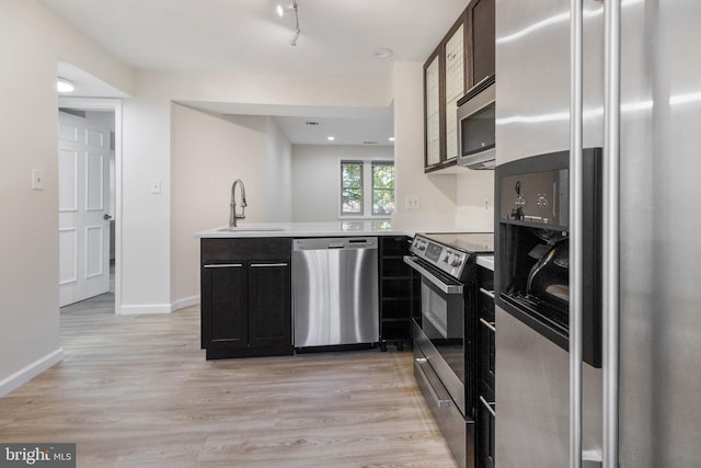 kitchen with a peninsula, a sink, appliances with stainless steel finishes, light wood-type flooring, and glass insert cabinets