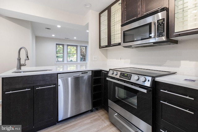 kitchen featuring light wood-style flooring, a peninsula, stainless steel appliances, light countertops, and a sink