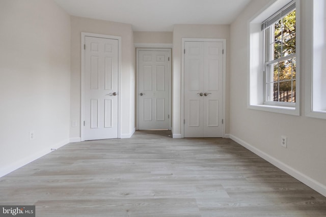 unfurnished bedroom featuring multiple closets, light wood-style floors, and baseboards