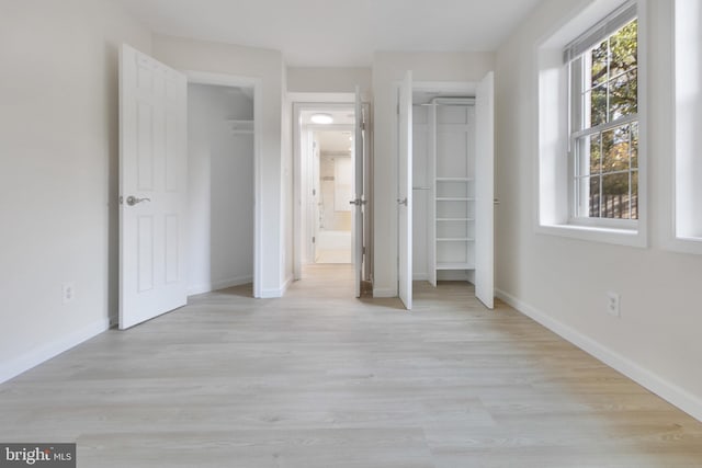 unfurnished bedroom with light wood finished floors, ensuite bath, and baseboards