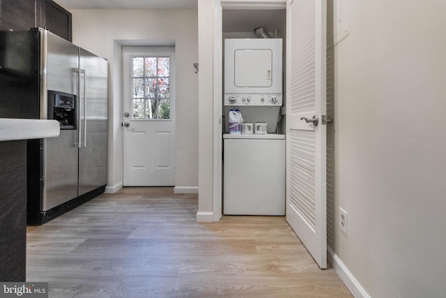 laundry area with baseboards, laundry area, light wood-style flooring, and stacked washer / drying machine