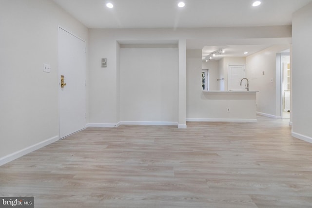 empty room with baseboards, a sink, light wood-style flooring, and recessed lighting