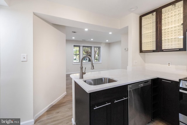 kitchen featuring a peninsula, dishwashing machine, dark cabinetry, and a sink