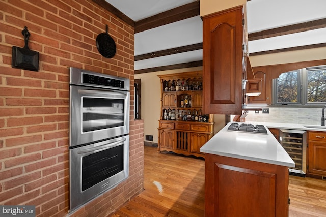 kitchen with stainless steel appliances, beverage cooler, sink, beam ceiling, and light hardwood / wood-style floors