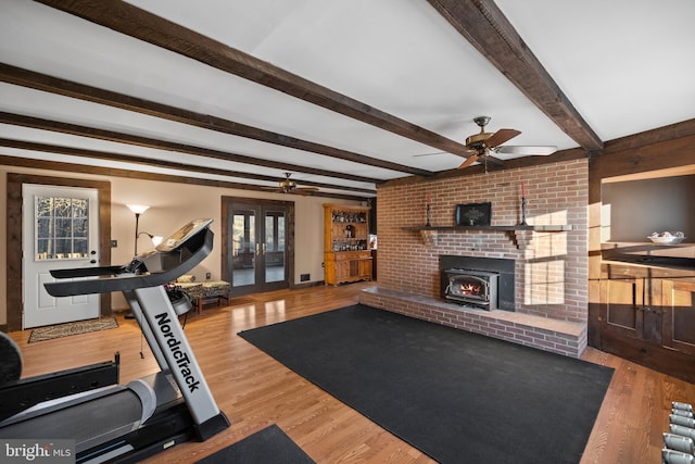 exercise room featuring ceiling fan, wood-type flooring, a wealth of natural light, and a wood stove