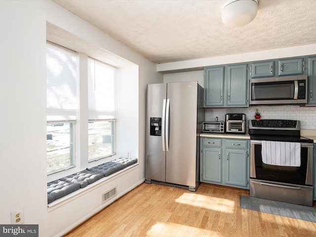 kitchen featuring plenty of natural light, a textured ceiling, appliances with stainless steel finishes, and decorative backsplash