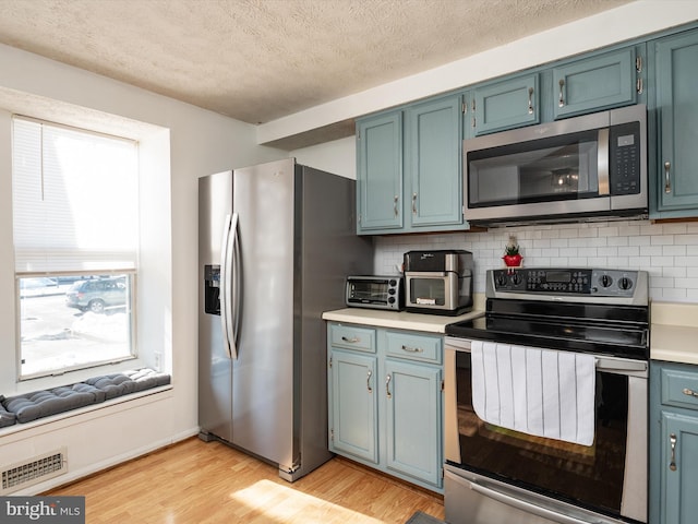 kitchen with light hardwood / wood-style floors, stainless steel appliances, blue cabinetry, a textured ceiling, and tasteful backsplash