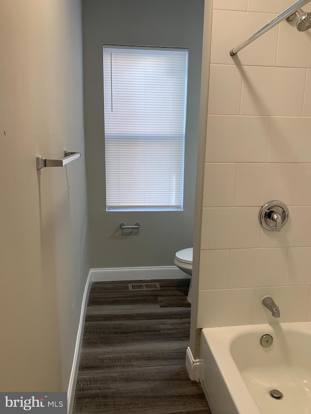 bathroom featuring wood-type flooring, tiled shower / bath combo, and toilet