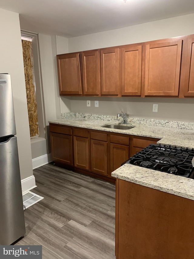 kitchen featuring light stone countertops, dark hardwood / wood-style floors, stainless steel refrigerator, and sink