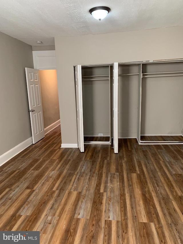 unfurnished bedroom with dark hardwood / wood-style flooring, a textured ceiling, and multiple closets