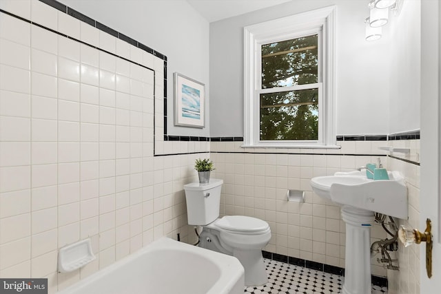 bathroom featuring sink, tile patterned flooring, toilet, a bathtub, and tile walls