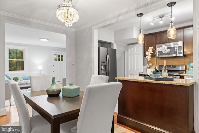 dining area with light hardwood / wood-style flooring, ornamental molding, and an inviting chandelier