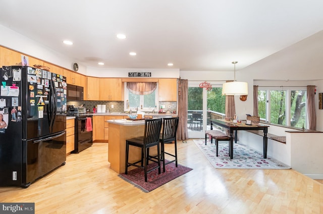 kitchen with backsplash, black appliances, a kitchen island, decorative light fixtures, and light hardwood / wood-style floors