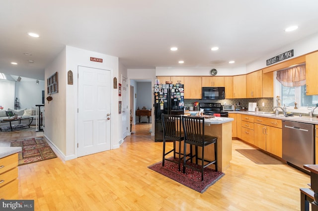 kitchen featuring a center island, black appliances, decorative backsplash, light wood-type flooring, and a breakfast bar area