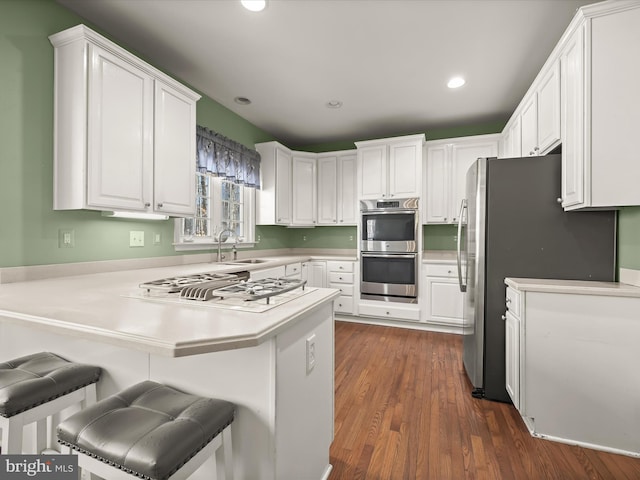 kitchen with sink, white cabinets, kitchen peninsula, a breakfast bar, and appliances with stainless steel finishes