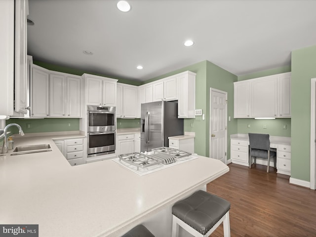 kitchen featuring sink, built in desk, appliances with stainless steel finishes, white cabinetry, and dark wood-type flooring