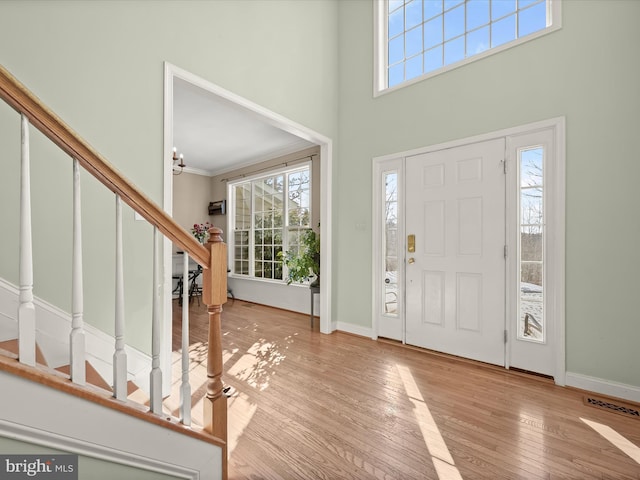 foyer entrance featuring crown molding, a notable chandelier, light hardwood / wood-style flooring, and a high ceiling