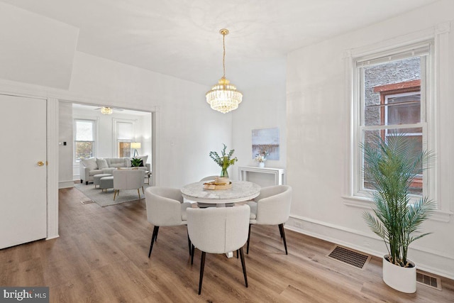 dining space with ceiling fan with notable chandelier and hardwood / wood-style flooring