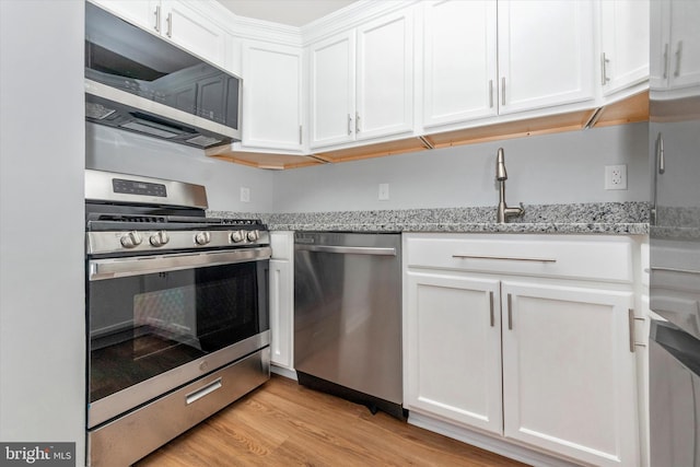 kitchen with white cabinets, light wood-type flooring, stainless steel appliances, and light stone countertops