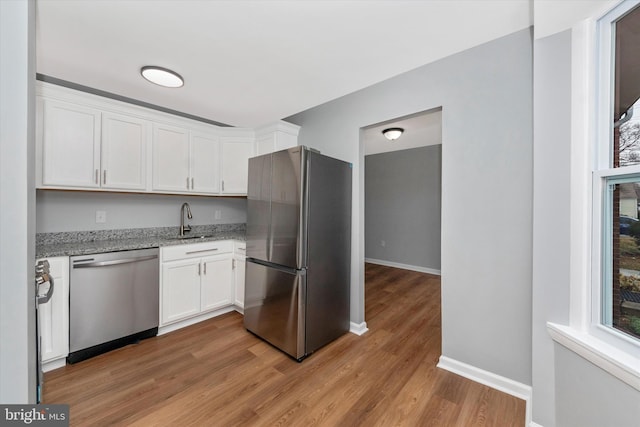 kitchen featuring appliances with stainless steel finishes, light stone counters, sink, light hardwood / wood-style flooring, and white cabinetry