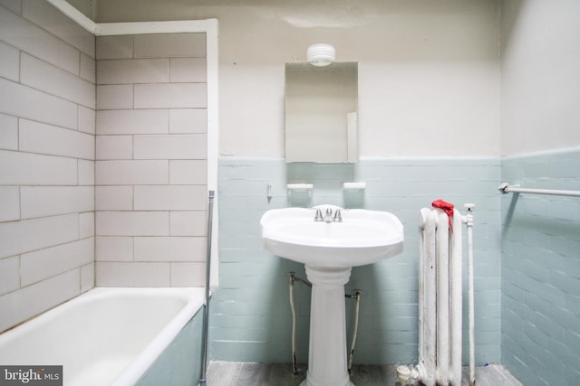 bathroom with hardwood / wood-style flooring, radiator heating unit, a tub to relax in, and tile walls