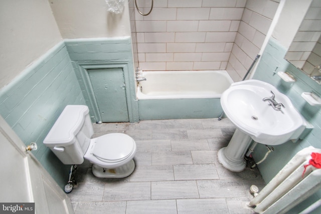 full bathroom with sink, toilet, tiled shower / bath, and tile walls