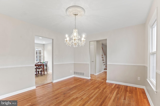 unfurnished dining area with a notable chandelier, wood-type flooring, and a healthy amount of sunlight