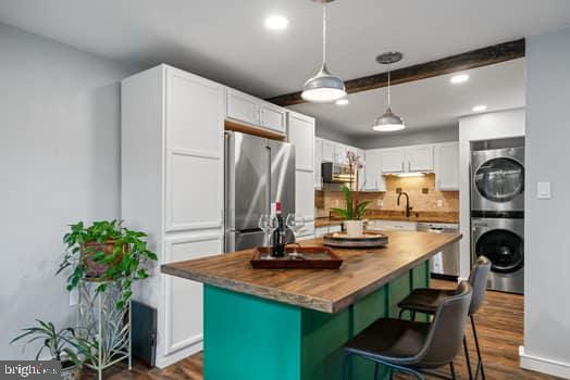 kitchen featuring butcher block counters, white cabinetry, a center island, stacked washing maching and dryer, and appliances with stainless steel finishes