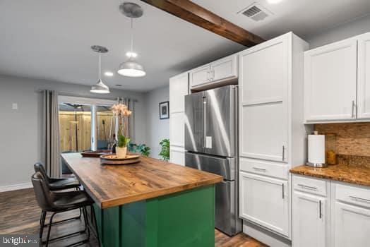 kitchen featuring stainless steel refrigerator, a center island, wooden counters, decorative light fixtures, and white cabinets