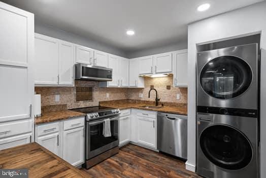 kitchen with appliances with stainless steel finishes, sink, stacked washer and dryer, white cabinetry, and dark hardwood / wood-style floors