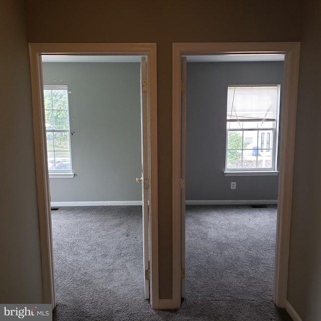 hallway featuring dark carpet and a wealth of natural light