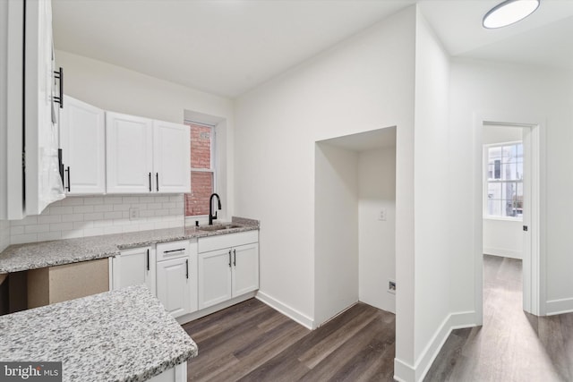 kitchen featuring light stone countertops, decorative backsplash, dark hardwood / wood-style flooring, sink, and white cabinetry