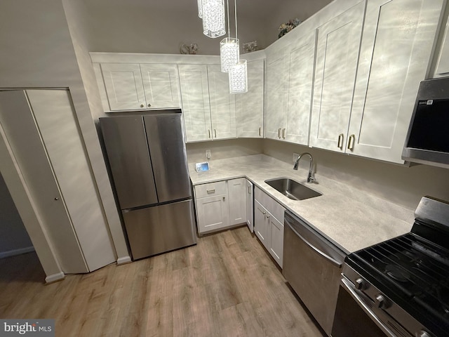 kitchen with white cabinetry, sink, light hardwood / wood-style floors, decorative light fixtures, and appliances with stainless steel finishes