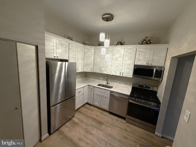 kitchen featuring appliances with stainless steel finishes, sink, pendant lighting, white cabinets, and light hardwood / wood-style floors