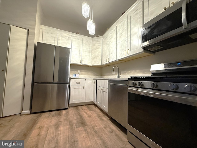 kitchen with stainless steel appliances, sink, decorative light fixtures, light hardwood / wood-style floors, and white cabinetry