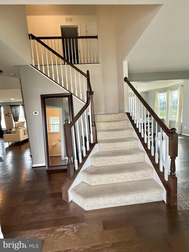 staircase with a towering ceiling and hardwood / wood-style flooring