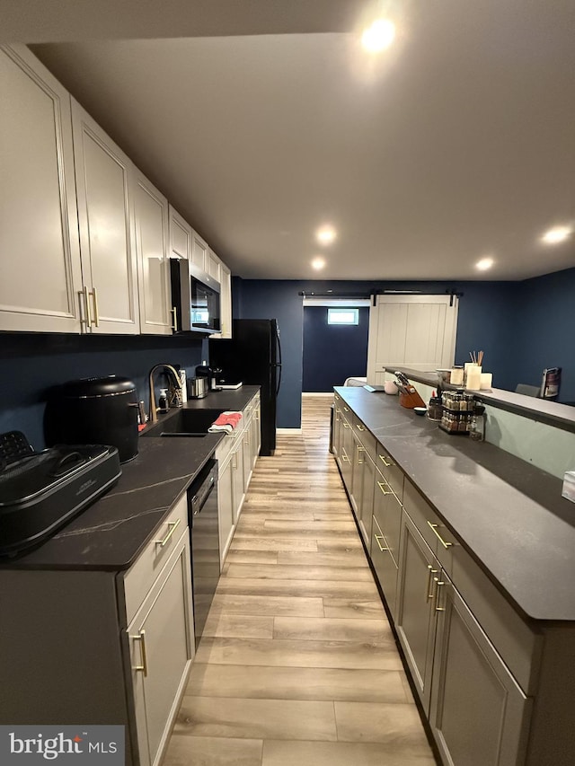 kitchen with sink, a barn door, light hardwood / wood-style flooring, white cabinets, and black appliances