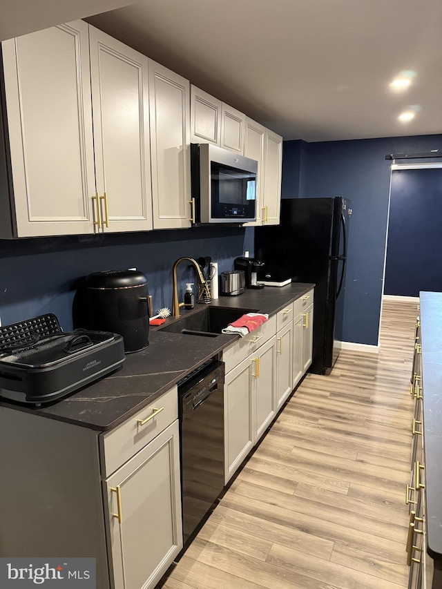 kitchen with white cabinets, dark stone counters, sink, dishwasher, and light hardwood / wood-style floors