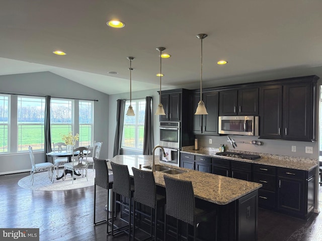 kitchen with appliances with stainless steel finishes, vaulted ceiling, a kitchen island with sink, sink, and pendant lighting